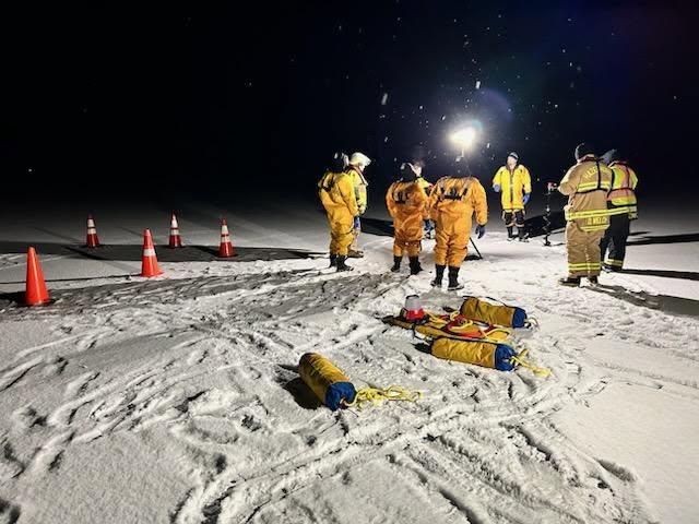 Responders in protective suits conducting a nighttime ice-rescue drill