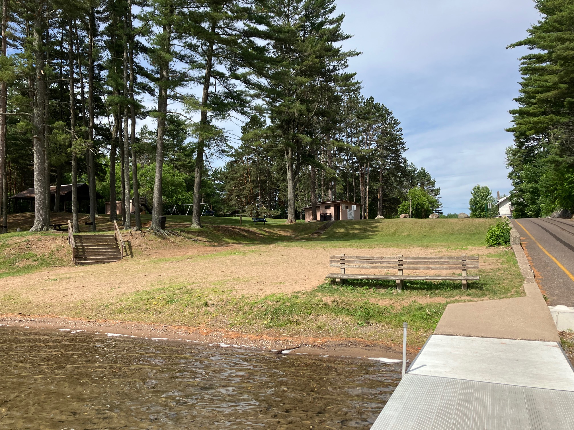 A sandy waterfront park with benches and a wooden dock beside the lake