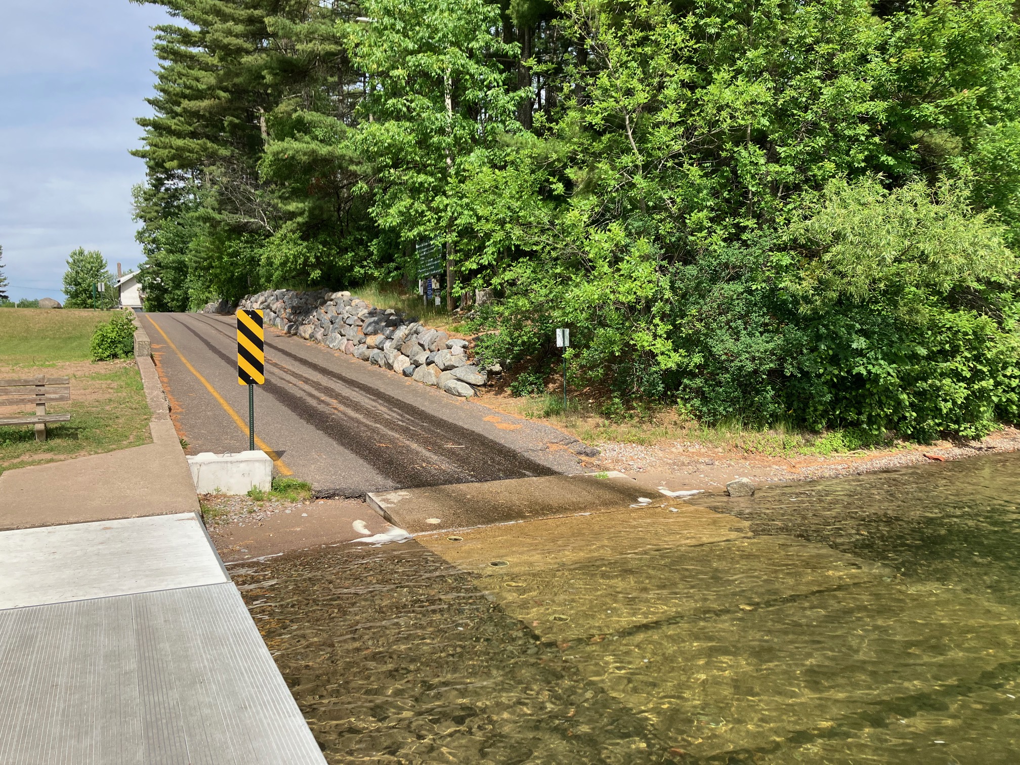 A paved access ramp descending through a wooded waterfront park